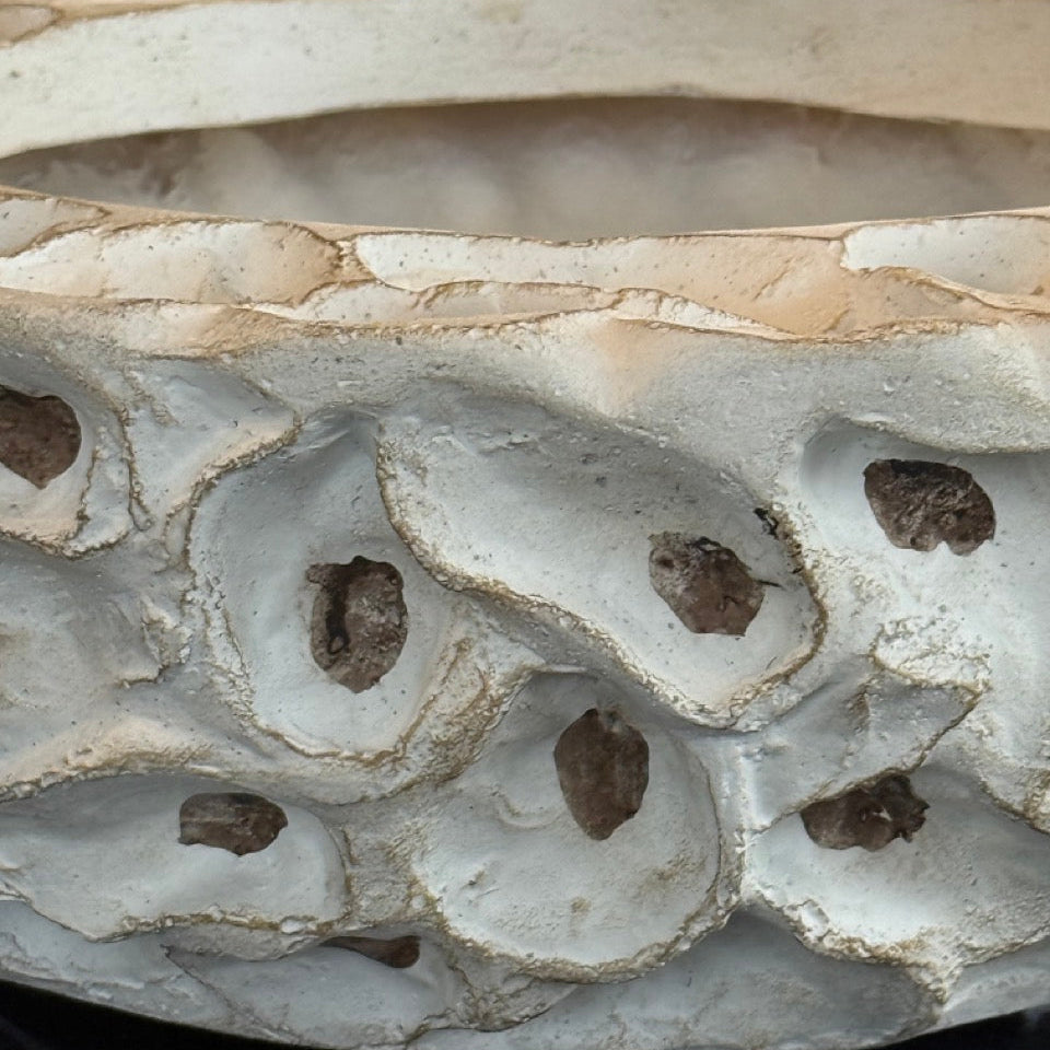 Decorative stone bowl with intricate carvings and holes on a dark surface.