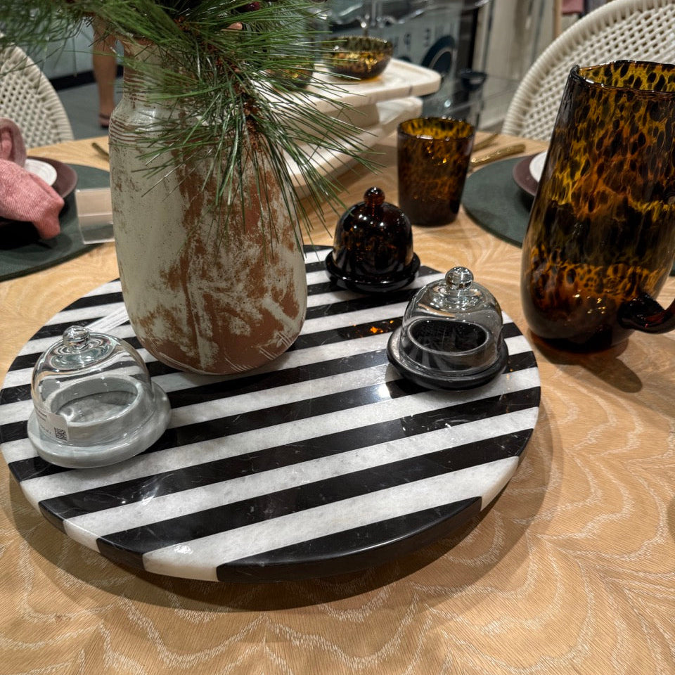 Decorative table setting with a black and white striped tray, glass vase, and decorative items.