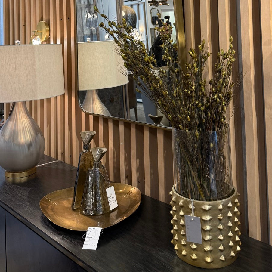 Decorative mirror on a console table with a lamp and vase in a room setting.