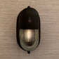 A black oval wall sconce with a ribbed clear glass shade, mounted on a textured beige wall.