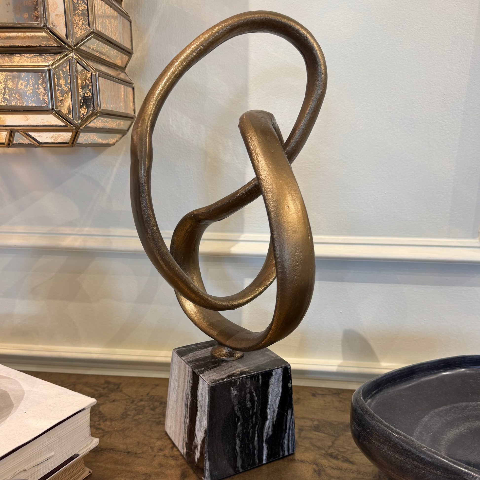 Bronze abstract sculpture on a marble base with decorative elements in the background