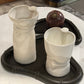 Two white ceramic vases on a black tray with a decorative object on a marble surface.