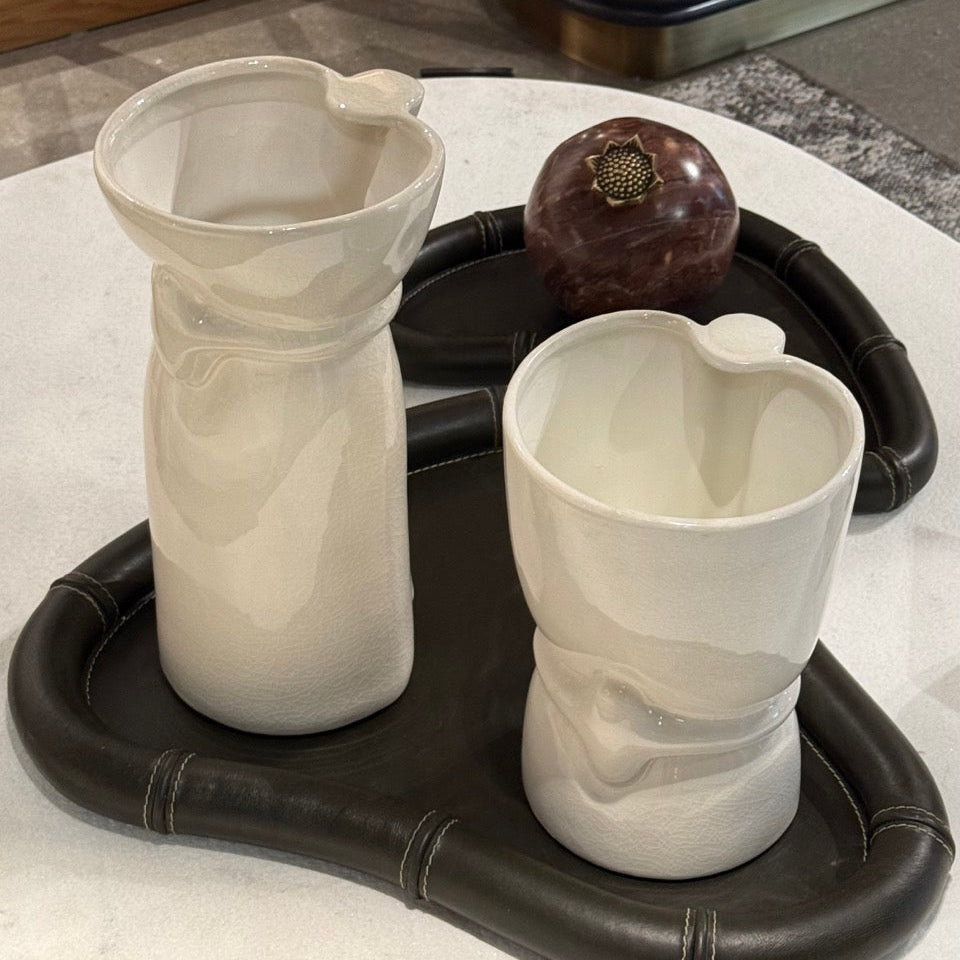 Two white ceramic vases on a black tray with a decorative object on a marble surface.