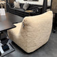 Beige textured armchair in a showroom setting with black furniture and decor.
