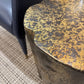 Close-up of a textured round table with a chair partially visible.