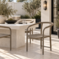 Outdoor patio dining set featuring a rectangular stone table and woven-back chairs in a modern backyard setting.