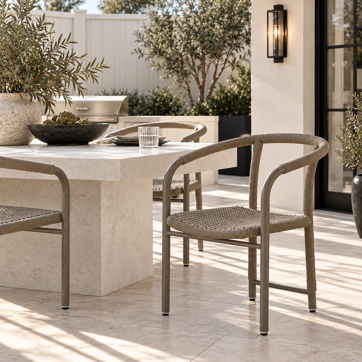 Outdoor patio dining set featuring a rectangular stone table and woven-back chairs in a modern backyard setting.