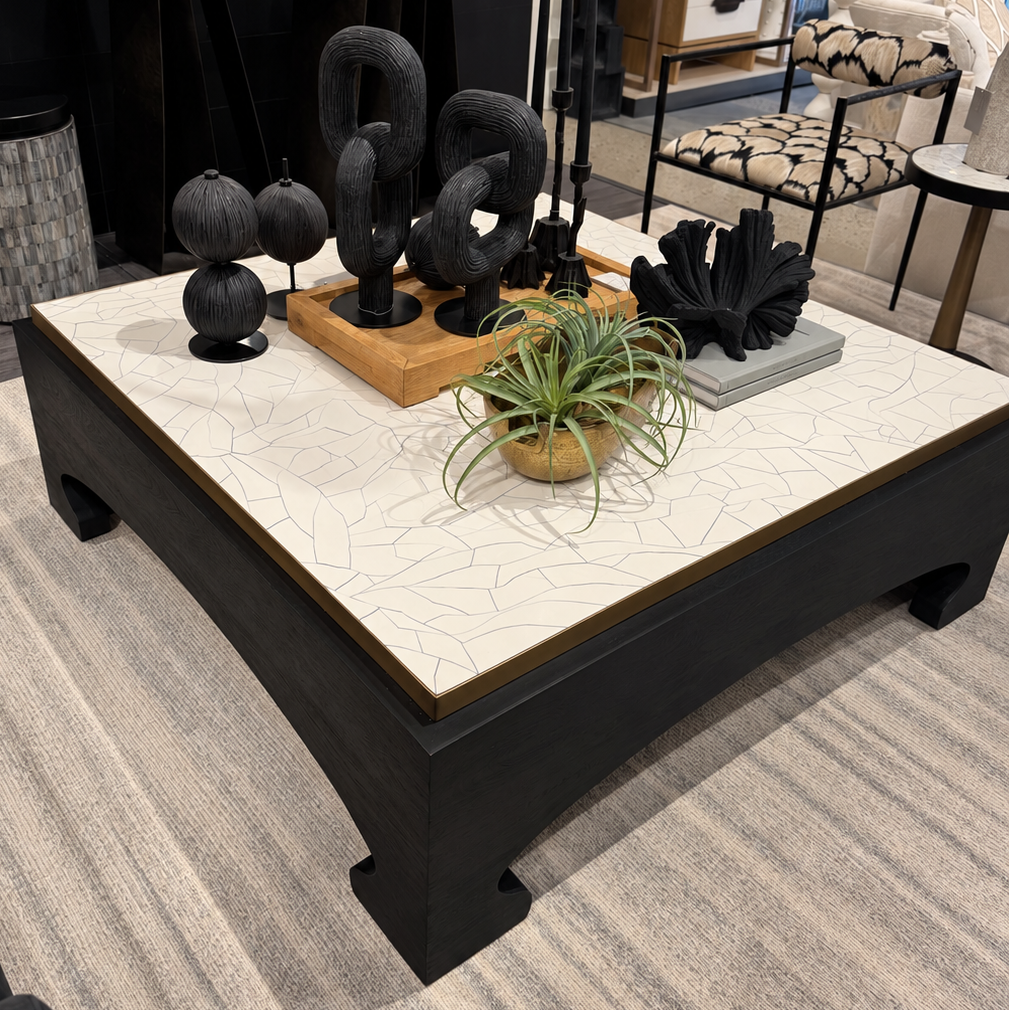 A modern square coffee table with a white marble-look top featuring a subtle crackle pattern and a dark wood base, styled in a contemporary living room setting.