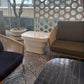 A modern outdoor lounge seating area featuring two wooden armchairs with dark blue and olive green cushions, a small white side table, a black tiled coffee table, and a decorative circular screen wall.
