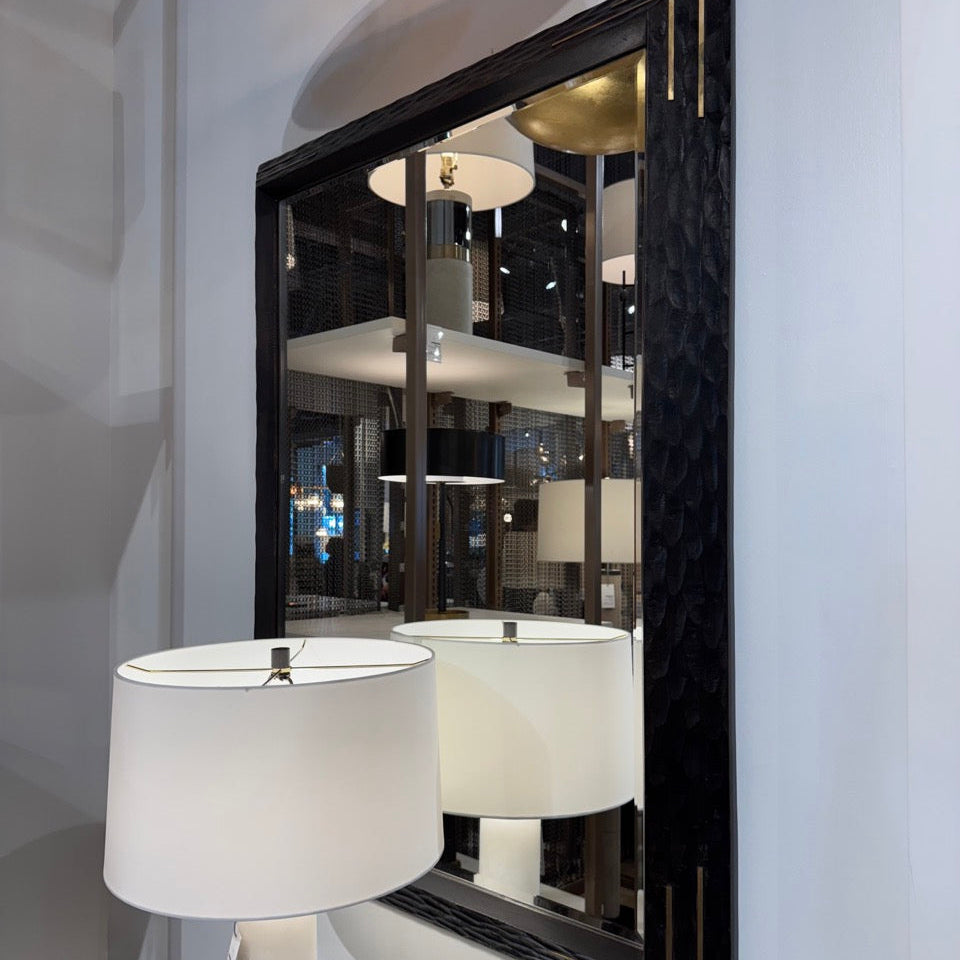 Decorative mirror with black frame on a wall with a lamp reflection