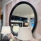 Round mirror with black frame on a wall with lamps and decor.