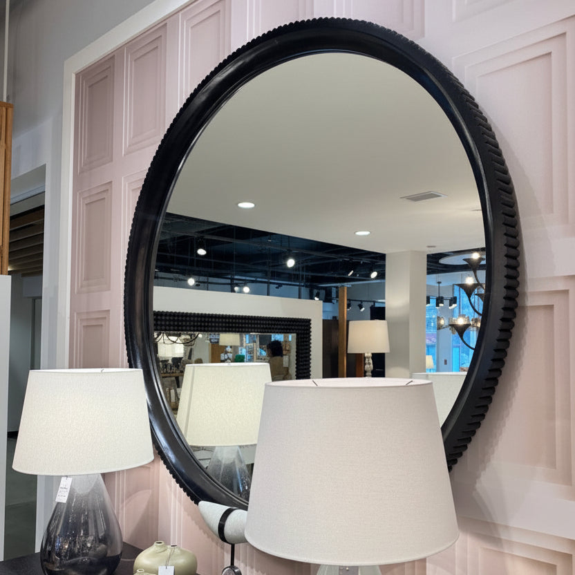 Round mirror with black frame on a wall with lamps and decor.