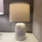 Table lamp with a textured base and beige shade on a surface.