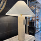 Table lamp with a beige base and white shade on a marble surface in an indoor setting.