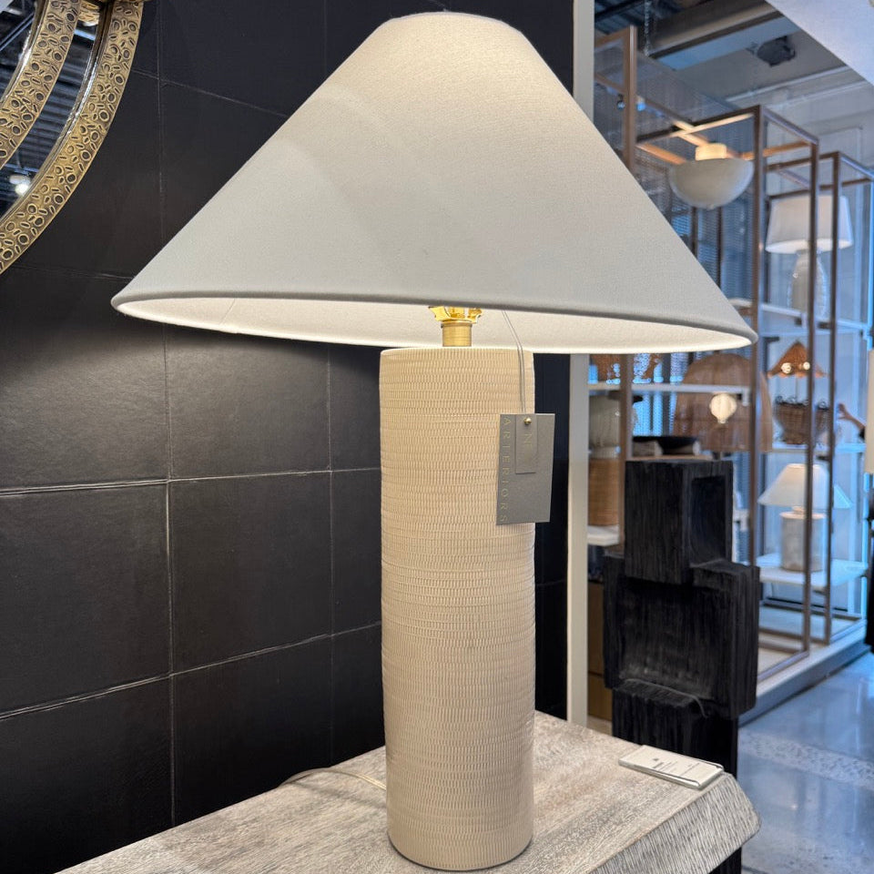 Table lamp with a beige base and white shade on a marble surface in an indoor setting.
