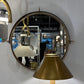 Round mirror with gold frame and brass lamp shade on a white wall.