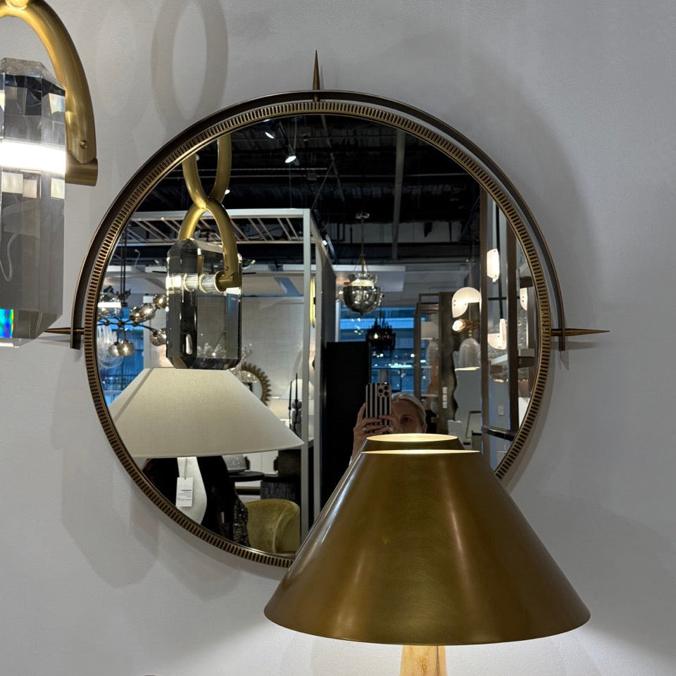 Round mirror with gold frame and brass lamp shade on a white wall.
