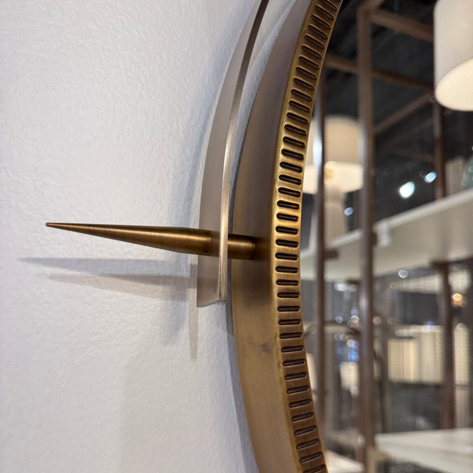 Gold wall clock with a modern design on a white wall.