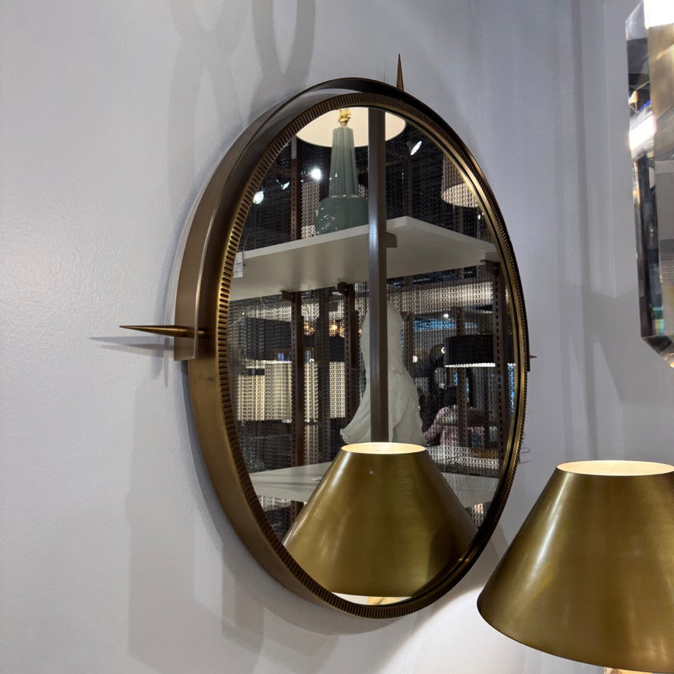 Round gold mirror with a lamp shade reflection on a white wall.