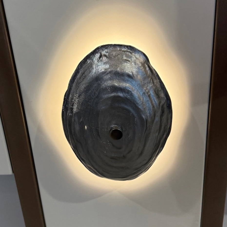 Decorative wall light fixture with a black, textured design on a white wall.