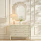 Decorative mirror above a dresser with a lamp and vase in a stylish room.