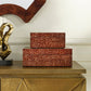 Two stacked rectangular decorative boxes with a red and beige animal-print pattern, displayed on a metallic gold console table against an off-white wall.