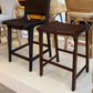 Two wooden stools with woven seats in a showroom setting.