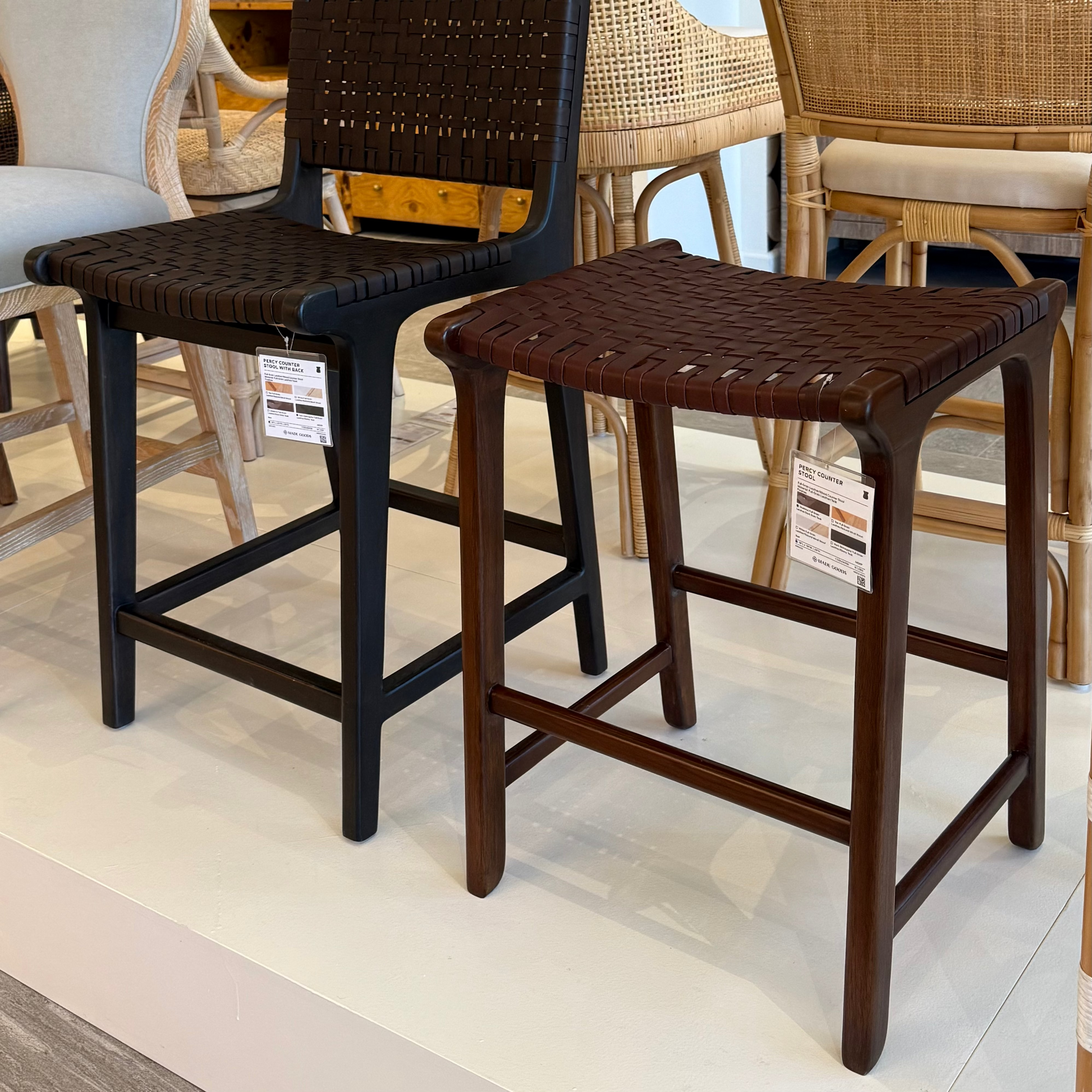 Two wooden stools with woven seats in a showroom setting.