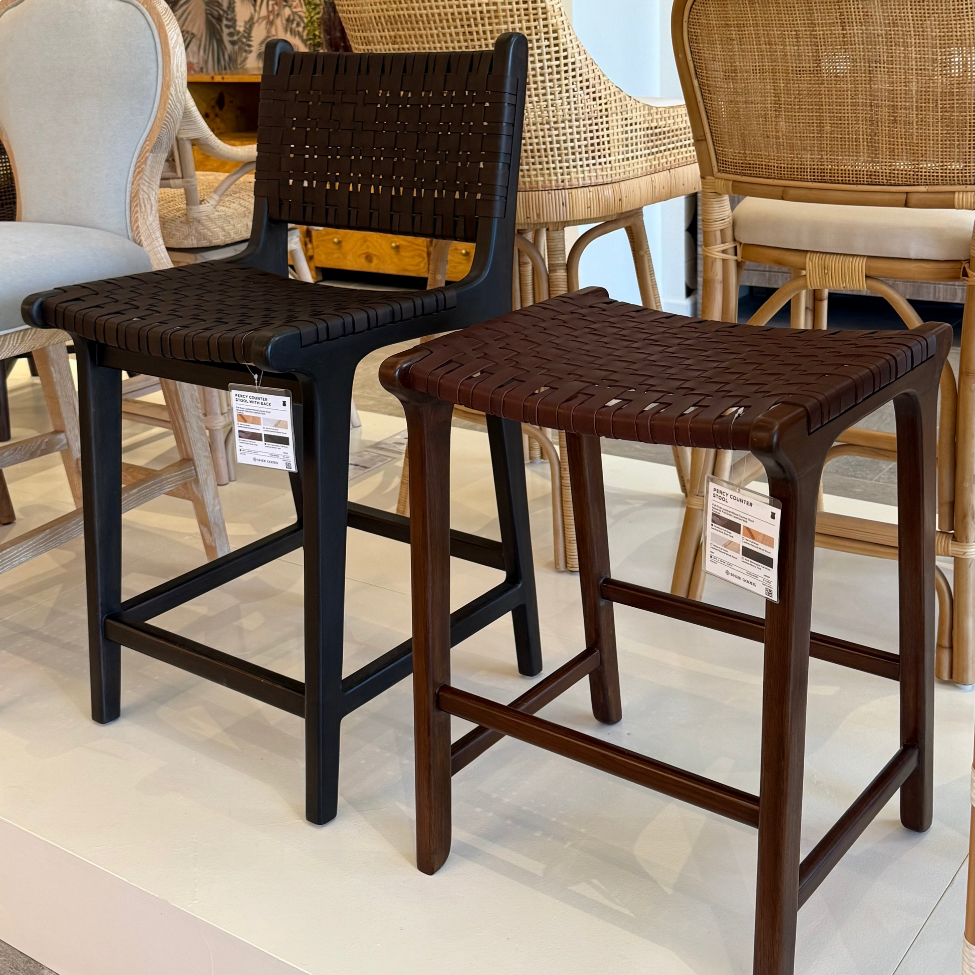 Two wooden stools with woven seats in a showroom setting.