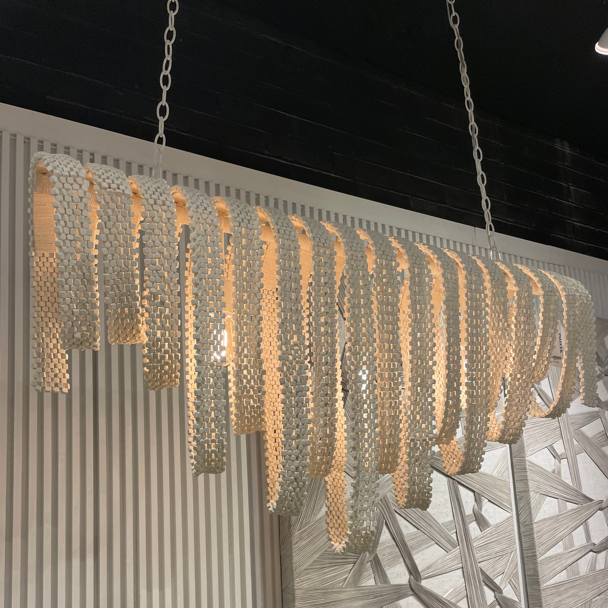 Decorative chandelier with a textured design on a table, surrounded by yarn balls and a plant.
