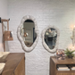 Bathroom with wooden vanity, mirrors, and decorative items against a white brick wall.