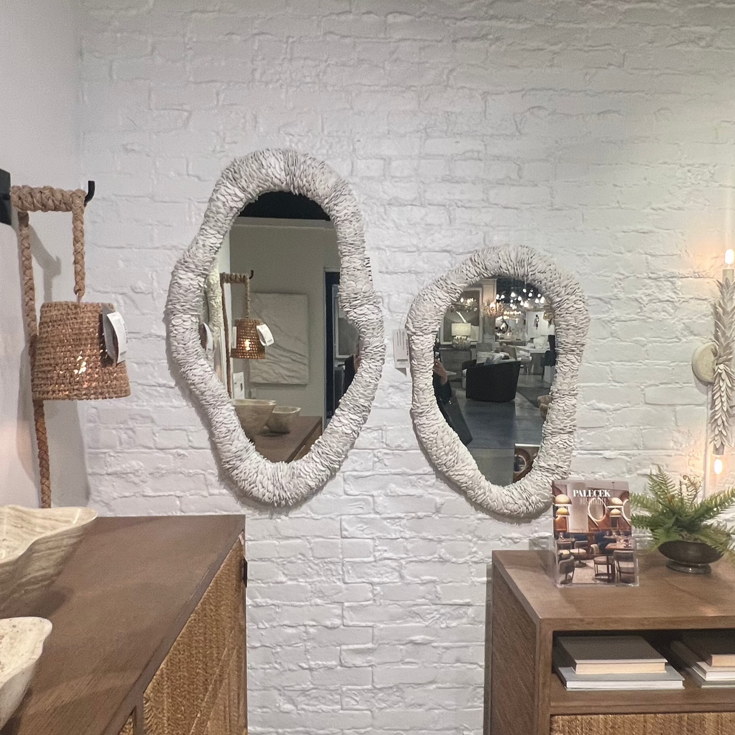 Bathroom with wooden vanity, mirrors, and decorative items against a white brick wall.