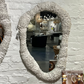 Round textured mirror on a white brick wall with a magazine titled 'Palecek' in the foreground.
