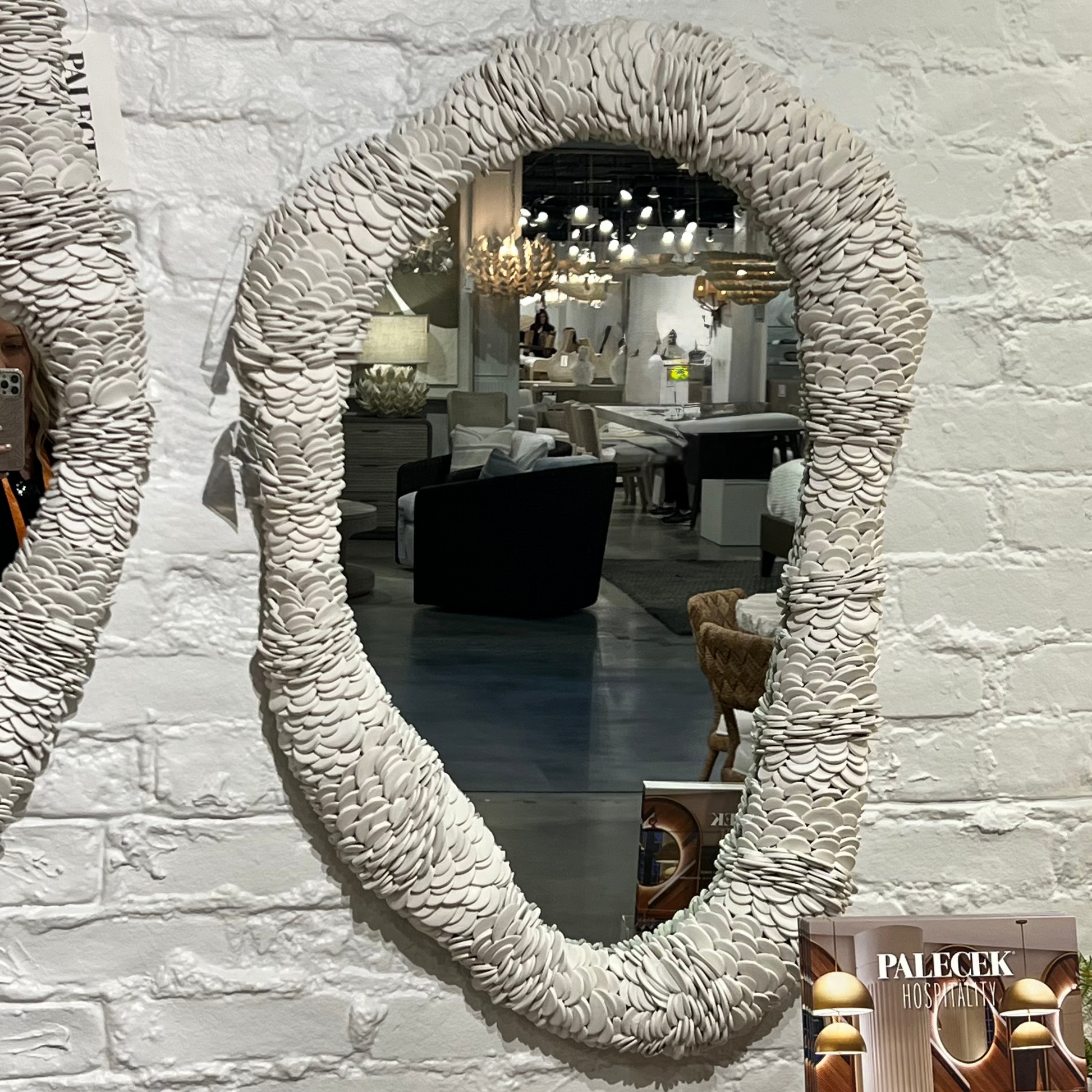 Round textured mirror on a white brick wall with a magazine titled 'Palecek' in the foreground.