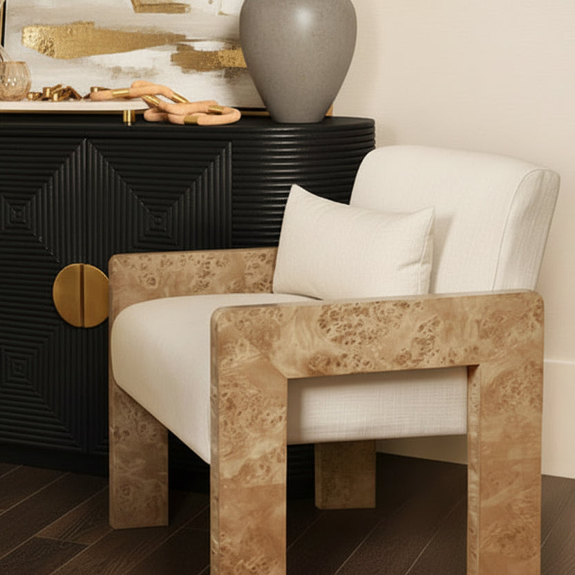 Modern chair with beige frame and white cushion next to a black sideboard with gold accents.