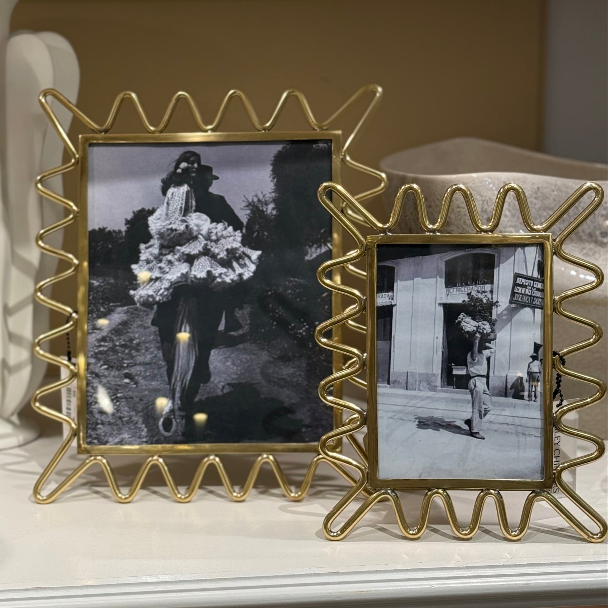 Gold decorative picture frames with black and white photos on a shelf.