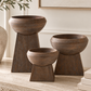 Three rustic dark brown wooden bowl planters on matching pedestal bases, arranged on a light stone surface in an indoor setting.