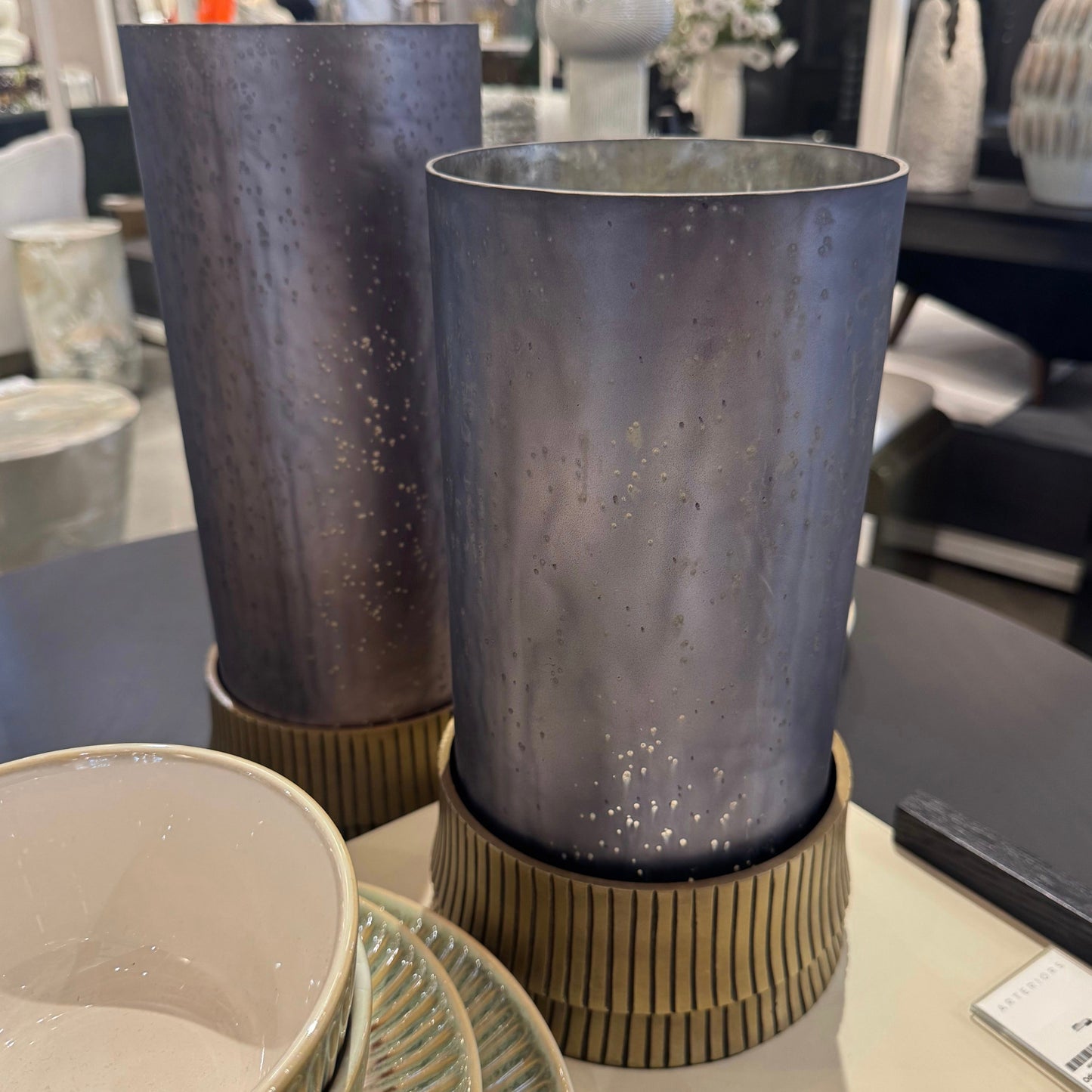 Two metallic vases on a table with a blurred store interior in the background