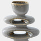 A ceramic sculptural vase or candle holder with a glossy speckled gray and gold glaze, featuring stacked rounded forms and oval cutouts, shown on a light gray background.