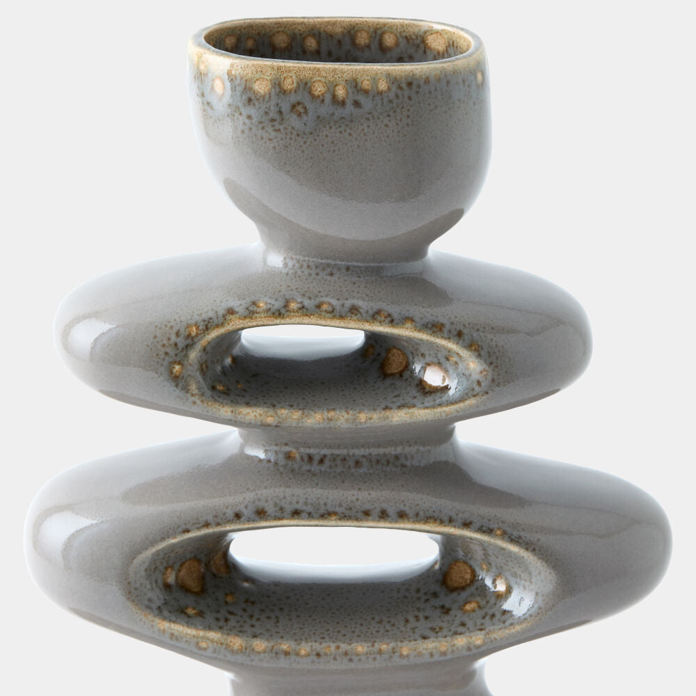 A ceramic sculptural vase or candle holder with a glossy speckled gray and gold glaze, featuring stacked rounded forms and oval cutouts, shown on a light gray background.