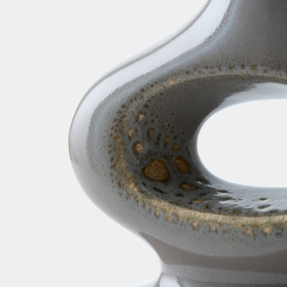 Close-up of a glossy ceramic vessel with a rounded, sculptural form and a small central opening, shown against a clean white background.