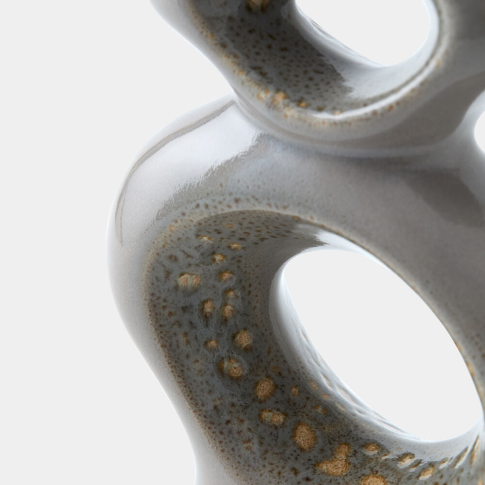 Close-up of a glossy ceramic sculptural vase with organic looped forms and speckled gold-brown oxidized details on a white background.