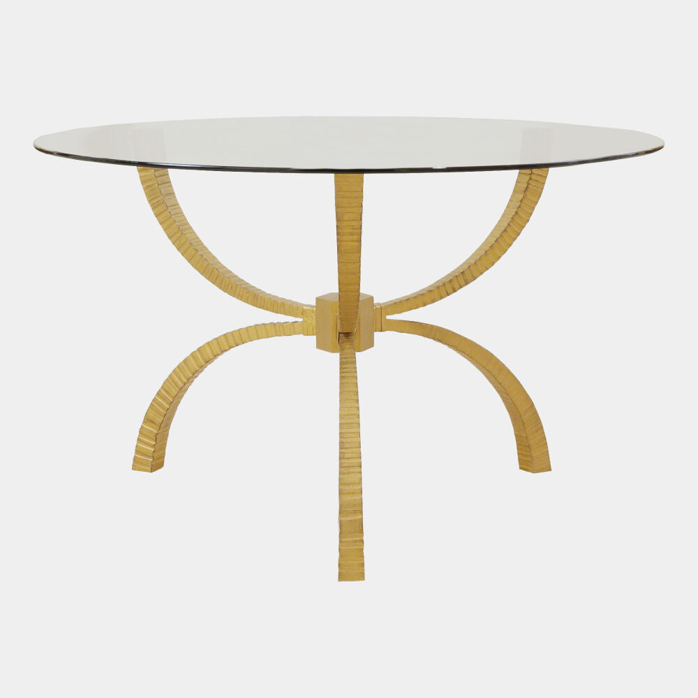 A round dining table featuring a clear glass top and a unique gold-colored metal base composed of five curved, ribbed legs that converge at the center, shown against a plain light gray background.