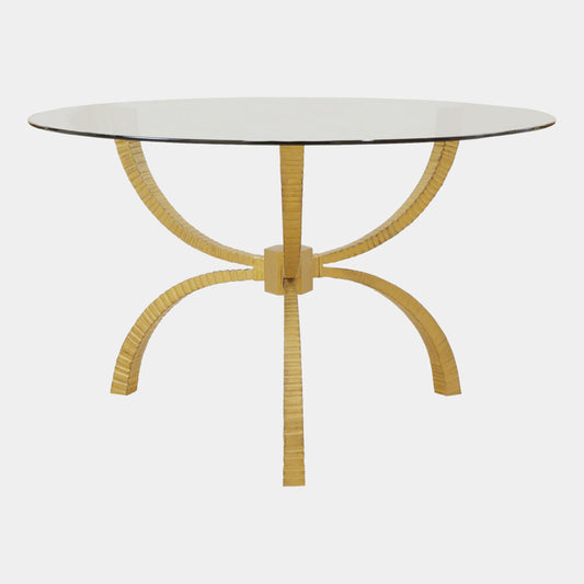 A round dining table featuring a clear glass top and a unique gold-colored metal base composed of five curved, ribbed legs that converge at the center, shown against a plain light gray background.