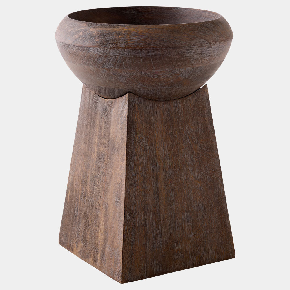 A dark brown wooden pedestal planter with a wide, rounded bowl on top of a tapered geometric base, shown against a plain light gray background.