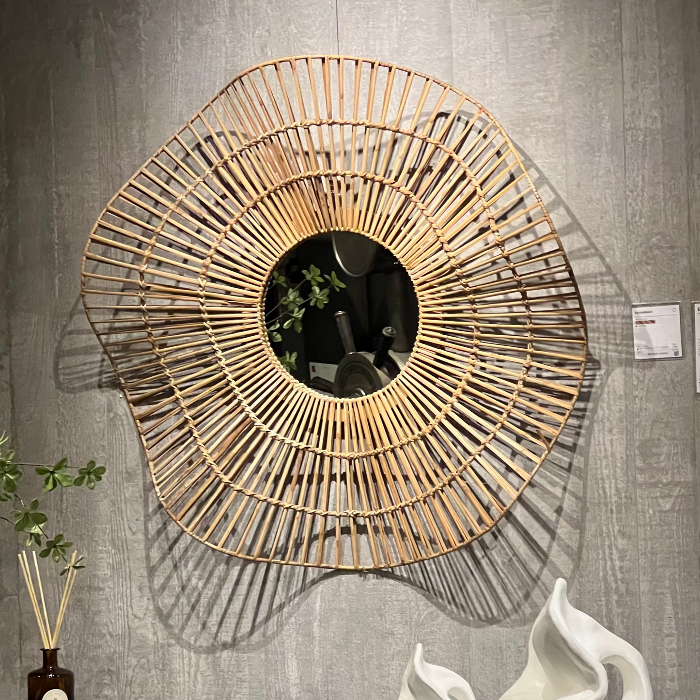 Decorative wall mirror with rattan-like frame on a gray wall with decorative items below.