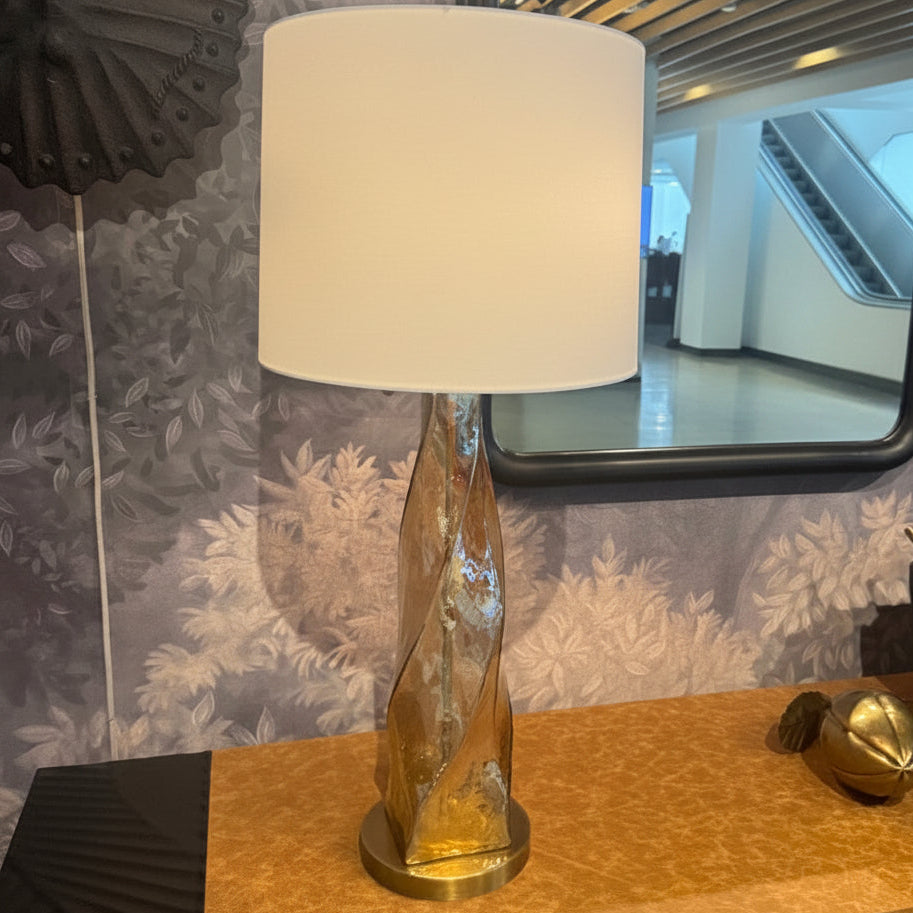 Decorative lamp on a table with a mirror reflecting people in a room.