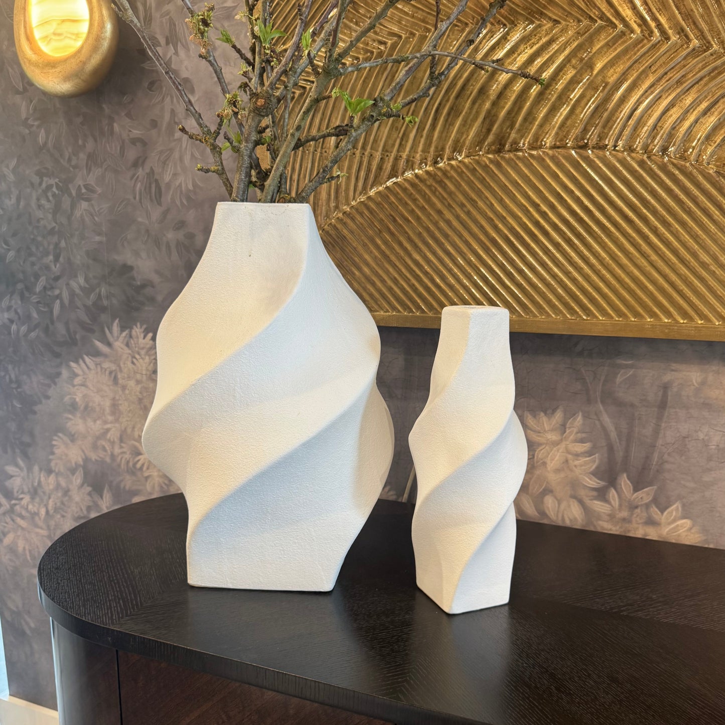 Two white abstract vases on a dark wooden surface with a textured wall in the background.
