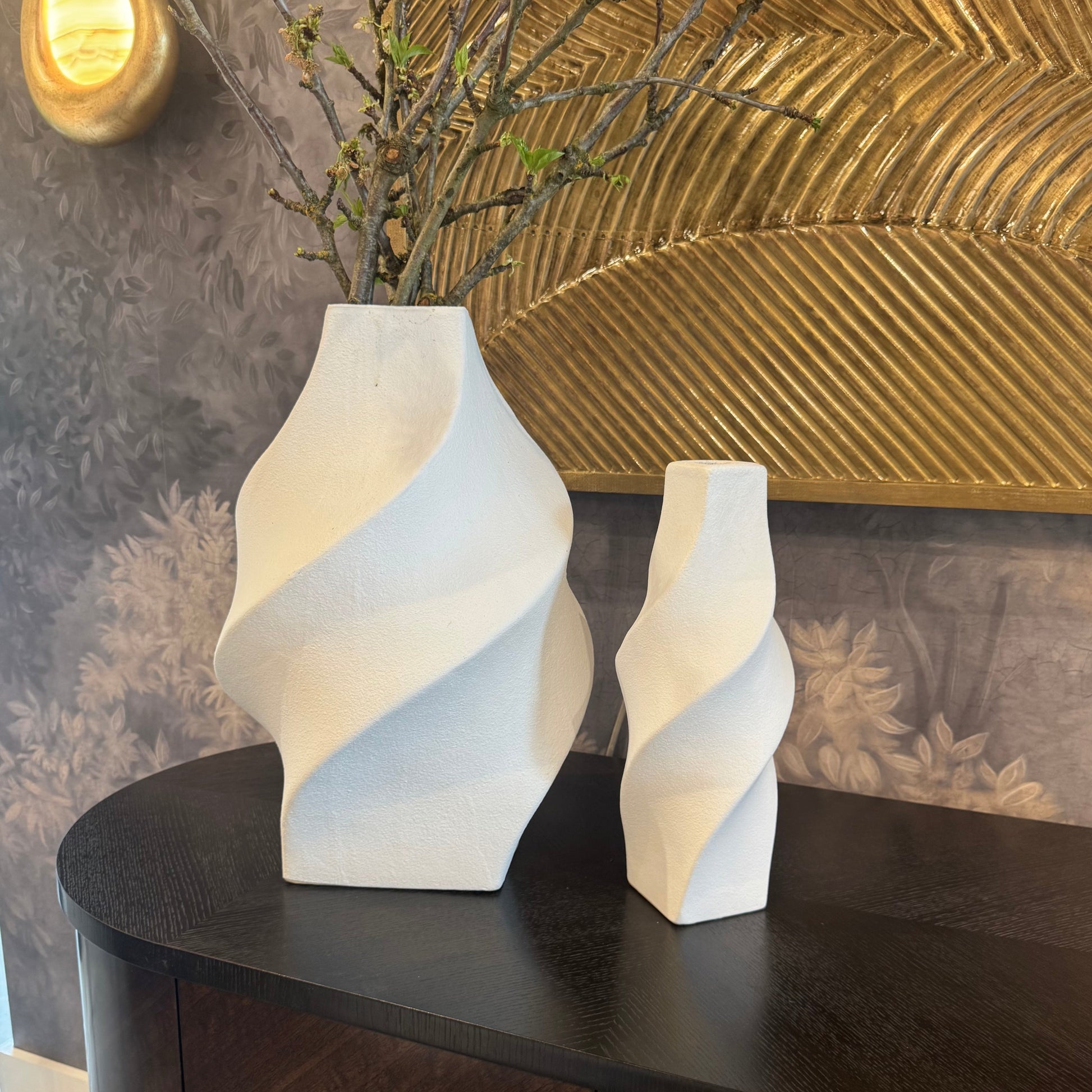 Two white abstract vases on a dark wooden surface with a textured wall in the background.