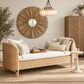 A woven rattan daybed with cream cushions and striped pillows, styled in a warm, neutral-toned living room with a matching rattan cabinet, a round sunburst mirror, and a hanging glass chandelier.